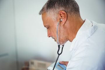 Medical professional listening with stethoscope while holding monitor against chest in clinic