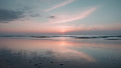 A tranquil beach scene during sunset with a vast, soft-toned sky and light clouds reflecting on a calm, reflective sea.