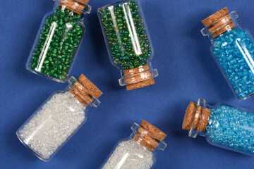 A collection of small glass bottles, each stoppered with a cork and filled with colorful seed...