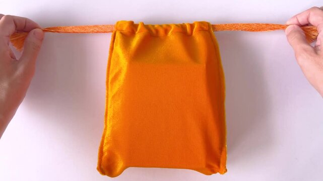 Asian woman's hands closing yellow velvet drawstring pouch on white tabletop background. Drawstring bag for make merit. Homemade. Bangkok, Thailand./ Slow down video
