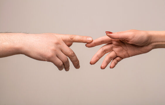 Woman and man touch finger at each other on grey background. Two gently stretched hands wishing to touch. Giving a helping hand to another. Two hands, helping arm of a friend, teamwork