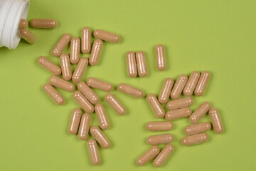 A top-down view of scattered beige-colored capsules spilling out of a white bottle on a light green...
