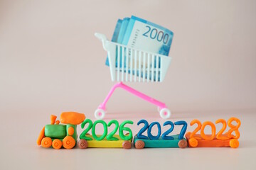 A toy train made of plasticine with the numbers 2026, 2027, 2028. Nearby is a shopping cart with...