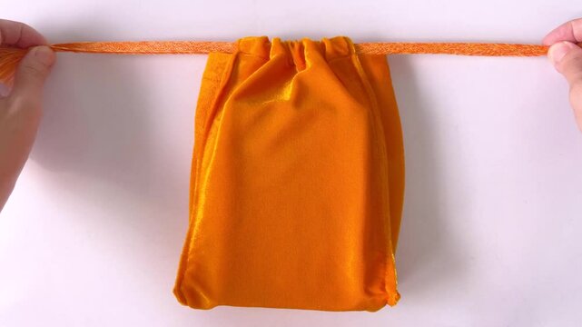 Asian woman's hands closing yellow velvet drawstring pouch on white tabletop background. Drawstring bag for make merit. Homemade. Bangkok, Thailand/ Slow down video