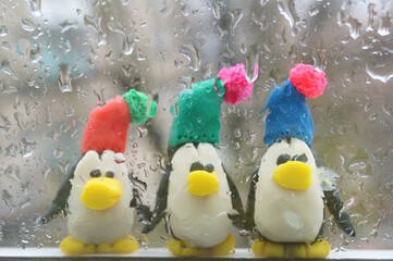 A penguin made of plasticine on the background of a wet rainy window.