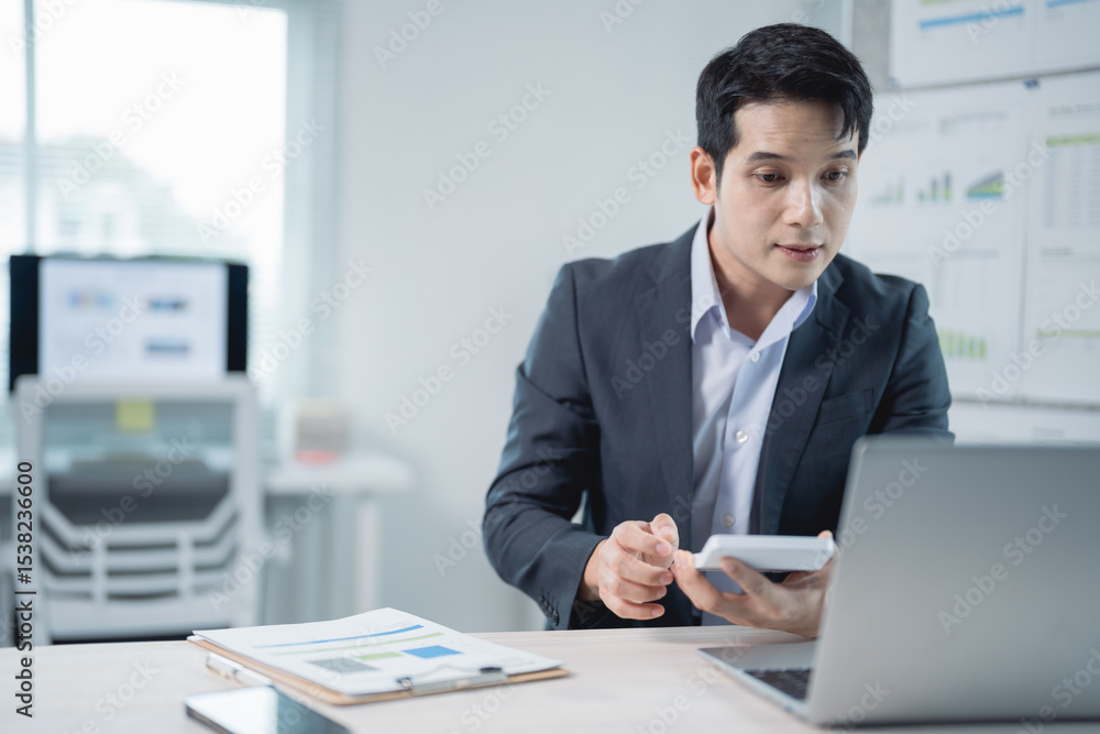 Poster businessman calculating and working on a laptop while reviewing documents in an office setting. dres