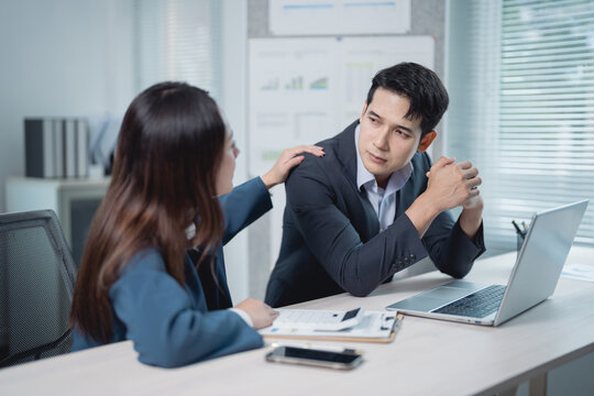 Asian businesspeople conversing at an office desk, with a businesswoman comforting a sad male colleague and offering support after job loss or business failure - Powered by Adobe