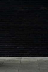 Minimalist urban backdrop: matte black brick wall with empty tiled pavement