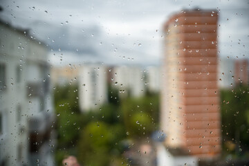 View of the city through wet glass with raindrops on the window in rainy weather on a summer day
