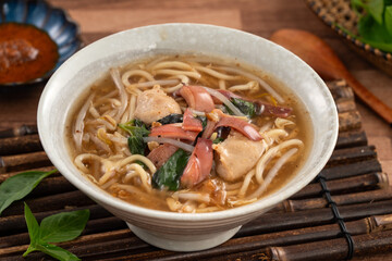 Taiwanese squid thick noodle soup in ceramic bowl on wooden table background.