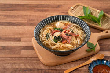 Taiwanese squid thick noodle soup in ceramic bowl on wooden table background.