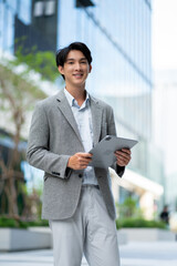 smiling happy successful asian businessman or lawyer in gray suit and blue shirt calling with his phone near his ear standing in front of an office building.Successful businessman holding mobile phone