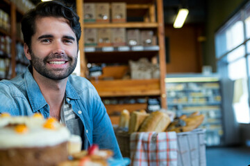 Smiling man wearing denim shirt tasting cake with fruit garnish at bakery table near bread baskets