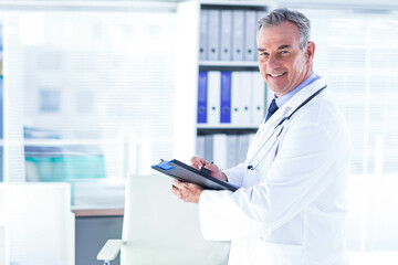Male doctor writing clipboard with pen in lab coat stethoscope at clinic by shelving, copy space