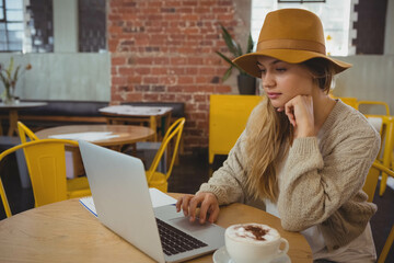 Woman typing on laptop while sitting at round wooden cafe table with cappuccino, copy space