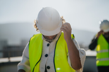 An architect adjusts their hard hat on a construction site, emphasizing safety and planning under...