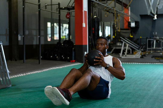 Fototapeta Man holding medicine ball and leaning back on turf inside fitness center with weight rigs behind