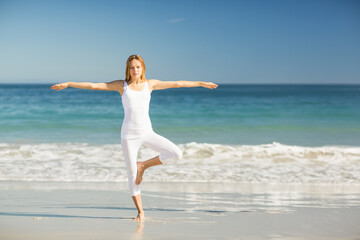 female practicing yoga tree pose at sandy shoreline wearing fitted tank top and cropped leggings
