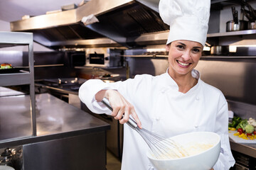 Wire whisk whisking creamy batter in large white bowl on steel workstation in commercial kitchen