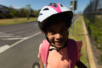 African American girl standing on suburban sidewalk wearing white-pink bicycle helmet and backpack