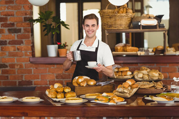 Male barista smiling behind pastry counter in café arranging pastries under globe pendant lights