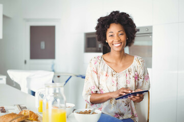 African American woman sitting at kitchen table holding tablet device by cereal bowls, copy space