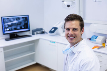 Male dentist standing by counter in treatment room with dental X-ray on monitor, copy space