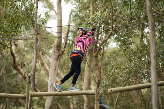 African American woman wearing harness balancing on beam holding overhead cable in ropes course