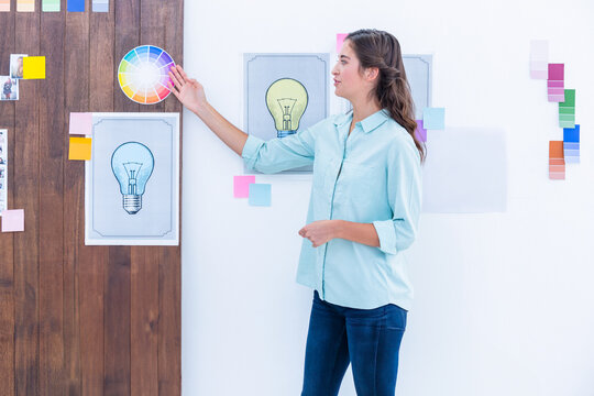 Female designer pointing at color wheel, sketches, sticky notes and swatches in studio