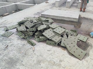 Green-painted steel brackets scattered on concrete floor at construction site, ready for structural...