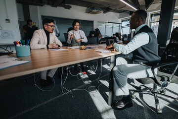 Three business employees engage in a collaborative meeting around a conference table in a modern office space, highlighting teamwork and discussion.