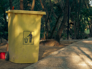 A dull yellow trash can in a park.