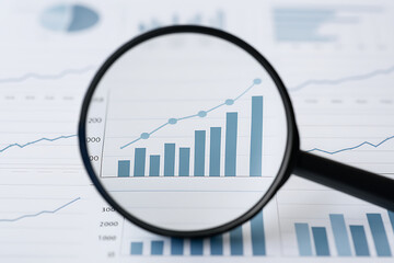 A close up of a magnifying glass over a bar graph and line graph showing an upward trend analysis view