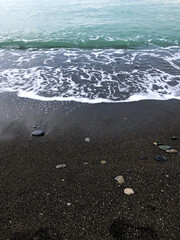 Black Sea coastline with dark sand, scattered stones, and turquoise water. Concept of natural coastal beauty, wild beaches, and the unique landscape of the Black Sea shore
