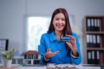 Smiling real estate agent presenting a credit card for a house purchase, with a house model...