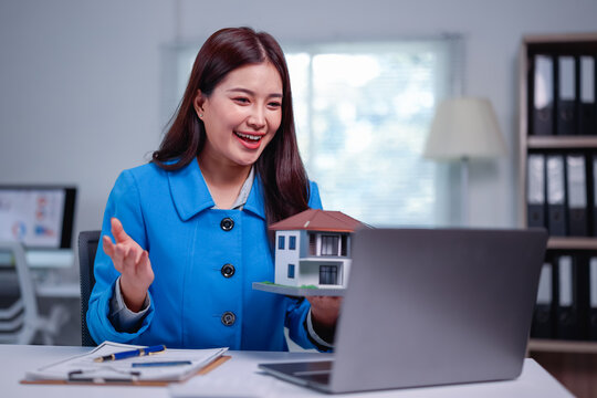 Smiling asian real estate agent showing house model during video conference with potential clients, discussing property details and offering investment opportunities