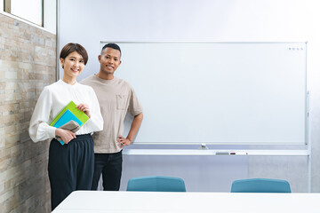 A black man and a Japanese woman standing in front of a whiteboard in a classroom