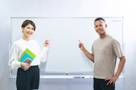 A black man and a Japanese woman pointing at a whiteboard in a classroom