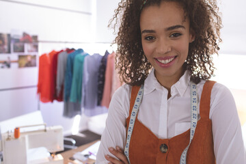 Fashion designer standing in studio wearing orange jumper with measuring tape, rack in background © wavebreak3