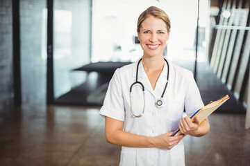 Stethoscope and file folder resting on concrete floor near glass partitions in clinic hallway