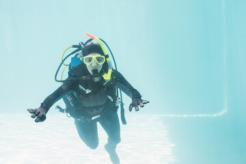 Scuba diver practicing underwater in clear pool, wearing full gear and yellow mask near tiled floor