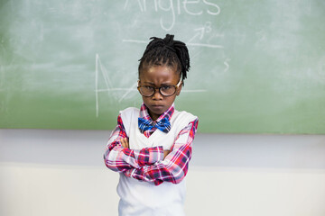 Schoolgirl is standing in front of green chalkboard with geometry diagrams and chalk dust on ledge