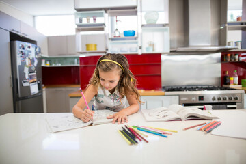 Girl child sitting at white countertop island in kitchen coloring workbook with colored pencils