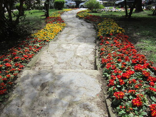 Colorful flowerbeds flank a winding stone path in a park.A well-maintained paved walkway winds...