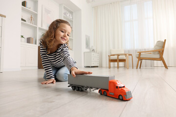 Little girl playing with toy car on floor at home
