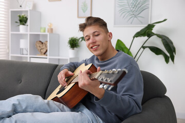 Happy man playing guitar on sofa indoors