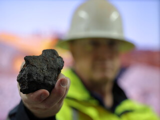 Manganese ore held by geologist, metallurgist, towards camera. Blurred background, differential focus. Mn mine, mining, critical mineral used in stainless steel and batteries