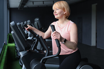 Senior woman training on elliptical machine in gym