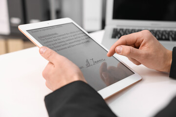 Electronic signature. Man using tablet at white table, closeup