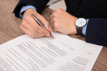 Man putting signature on document at wooden table, closeup